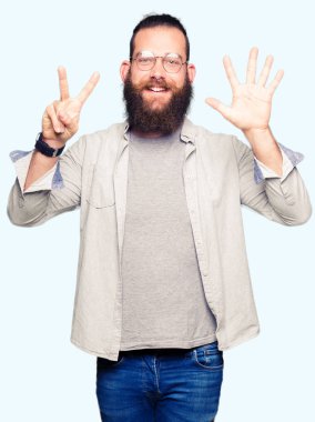 Genç sarışın adam gösteren gözlük giyen ve parmak sayısı yedi ile işaret ederken emin ve mutlu gülümseyen.