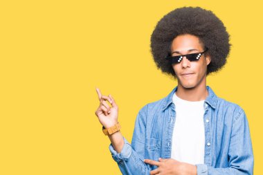 Thug hayat kocaman bir gülümseme ile yüzünde, gözlüklü afro saçlı genç Afro-Amerikan adam kameraya bakarak yan el ve parmak ile işaret.