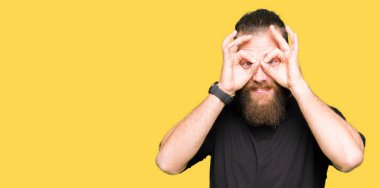 Dilini, parmaklarının arasından baktığını yapışmasını dürbün gibi ok jest yapıyor rahat t-shirt giyen genç sarışın adam. Deli ifade.