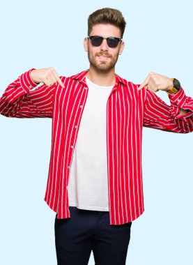 Yüzünde gülümseme ile kendinden emin görünüyorsun, kendini gururlu ve mutlu parmakları ile işaret giyen güneş gözlüğü genç yakışıklı adam.