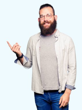 Yüzünde büyük bir gülümseme ile gözlük giyen genç sarışın adam, kamera bakarak yan el ve parmak ile işaret.