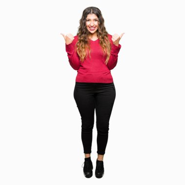 Kırmızı kazaklı başarı işareti el ile pozitif jest yapıyor giyen genç güzel kadın başparmak gülümseyen ve mutlu. Neşeli bir ifadeyle, kazanan jest kameraya bakıyor.