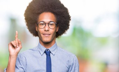 Afro saçlı gösterilen ve kendinden emin ve mutlu gülümseyen bir parmak ile işaret eden oktan yukarı gözlüklü genç Afro-Amerikalı iş adamı.