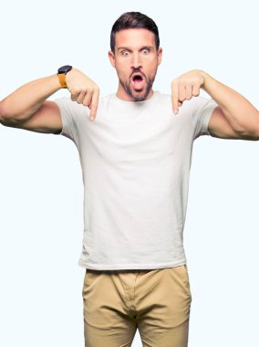 Casual beyaz t-shirt işaret parmakları ile reklam, sürpriz yüz ve açık ağız gösterilen giyen yakışıklı adam