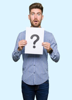 Genç yakışıklı bir soru işareti bir sürpriz yüz, korkuyor ve heyecanlı korku ifadesi ile şok korkmuş ile holding Kağıt adam