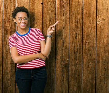 Kameraya bakarak yan el ve parmak ile işaret yüzünde kocaman bir gülümseme ile izole arka plan üzerinde gözlük güzel genç Afro-Amerikan kadın.