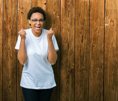 Güzel genç Afro-Amerikan kadın izole arka plan üzerinde kutluyor gözlük takan şaşırttı ve silah ile başarı için yükseltilmiş ve açık gözler hayrete düşürdü. Kazanan kavramı.