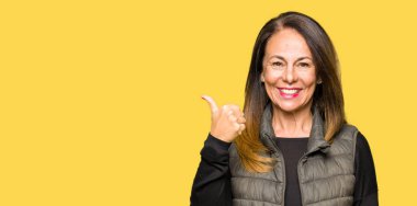 Mutlu yüz görünümlü ve başparmak yukarı ile yan işaret gülümseyen kış yelek giyen güzel orta yaş kadın.