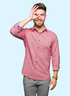 Genç yakışıklı iş casual adam gülümsüyor, parmakları ile mutlu yüz üzerinden seyir göz el ile ok jest yapıyor.