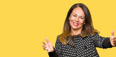 Sarılmak için kollarını açarak gülümseyerek kameraya bakarak moda ceket giyen güzel orta yaş kadın. Neşeli ifade kucaklayan mutluluk.