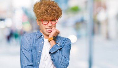 Yakışıklı genç afro saçlı gözlüklü stresli ve gergin elle çivi ısırma ağzına bakıyor. Anksiyete sorunu.