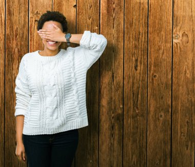 Gülümsüyor ve gözleri için sürpriz kapsayan yüz el ile gülüyor izole arka plan üzerinde kazak giyen güzel genç Afro-Amerikan kadın. Kör kavramı.