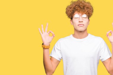 Afro saç ile genç yakışıklı adam gözlük giymek rahatlayın ve gözleri ile gülümseyen meditasyon jest parmaklar ile kapalı. Yoga konsepti.