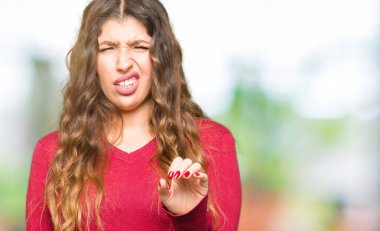 Kırmızı kazak giyen genç güzel kadın tiksinti ifadesi, memnun ve korkulu tiksinti yüz yapıyorsun çünkü nefret tepki. Elleriyle kaldırdı. Sinir bozucu kavramı.