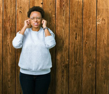 Yüksek sesle müzik gürültü rahatsız ifade parmaklarıyla kulaklarıyla kapsayan izole arka plan üzerinde gözlük takan genç güzel Afrikalı-Amerikalı kadın. Sağır kavramı.