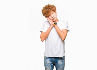 Afro saç ile genç yakışıklı adam rahat beyaz t-shirt uyku yorgun hayal ve el ile poz kapalı gözleri ile gülümseyen süre uyuyan.