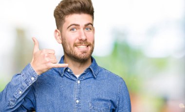 Casual kot gömlek gülümseyen giyen genç yakışıklı sarışın adam el ve parmak telefonda konuşmak ile telefon jest yapıyor. Kavramları iletişim.