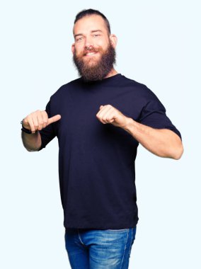 Rahat t-shirt giyen genç sarışın adam yüzünde gülümseme ile kendine güvenen görünümlü, parmaklarıyla gurur ve mutlu kendini işaret.