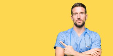 Yakışıklı Doktor adam tıbbi üniforma izole üzerinde arka plan işaretçi el parmak tarafı gösteren reklam, ciddi ve sakin yüz için