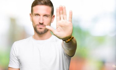 Yakışıklı adam rahat beyaz t-shirt giyen elin avuç ile şarkı stop yapıyor. Negatif ve ciddi bir jest yüz ifadesiyle uyarı.