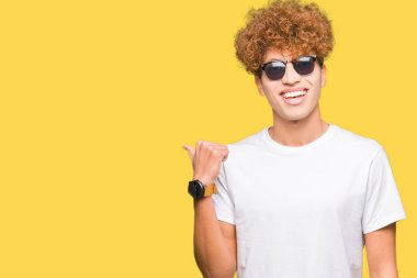 Seyir ve başparmak yanında yukarıyı mutlu yüz ile gülümseyen güneş gözlüğü takıyor afro saçlı Genç yakışıklı adam.