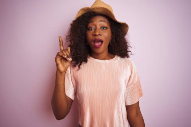 Genç Afro-Amerikalı kadın tişört ve şapka giyip izole edilmiş pembe arka plan üzerinde başarılı bir fikir işaret ediyor. Heyecanlı ve mutlu. Bir numara..
