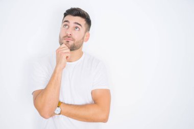 Beyaz tenli arka plan üzerine günlük beyaz tişört giyen genç yakışıklı bir adam. Elleri çenesinde soru sorarken, düşünceli bir ifade takınıyor. Düşünceli bir yüzle gülümsüyor. Şüphe kavramı.
