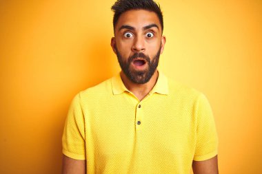 Sarı arka plan üzerinde duran polo giyen genç Hintli adam korku, korku ve heyecan dolu yüz ifadesiyle korkmuş ve şok olmuştu..