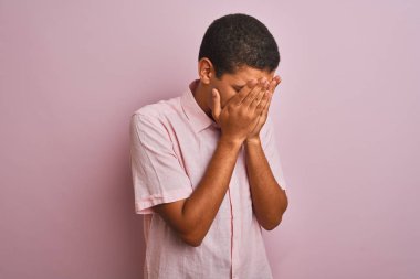 Genç, yakışıklı Arap adam, günlük gömleğini giymiş, pembe arka planda dikiliyor, üzgün bir ifadeyle elleri ile yüzünü kapatıyor, ağlarken. Depresyon kavramı.