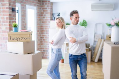 Karton kutuların etrafında duran genç ve güzel bir çift şüpheci ve gergin, kollarını kavuşturmuş yüz ifadesini onaylamıyor. Negatif kişi.