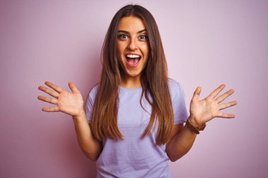 Genç ve güzel bir kadın, izole edilmiş pembe arka planda dikilip kollarını kaldırıp heyecanla haykırarak başarıyı kutluyor. Kazanan konsept