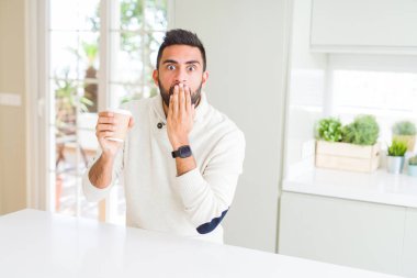 Yakışıklı İspanyol bir adam kağıt bardakta kahve içiyor ağzı kapalı bir şekilde hata yaptığı için utanmış, korku ifadesi, sessizlikten korkmak, gizli bir konsept.