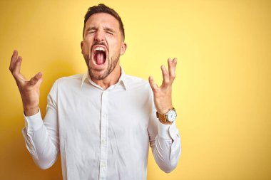 Sarı izole edilmiş arka plan üzerinde zarif beyaz gömlek giyen genç yakışıklı adam kollarını kaldırmış ve gözlerini kapatmış heyecanla haykırarak başarının çılgınlığını kutluyor. Kazanan konsept