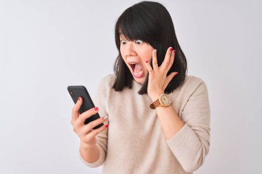 Genç ve güzel Çinli bir kadın, izole edilmiş beyaz arka planda dururken mutlu ve heyecanlı, kazanan yüz ifadesi zaferi büyük bir gülümsemeyle kutluyor ve ellerini kaldırıyor.