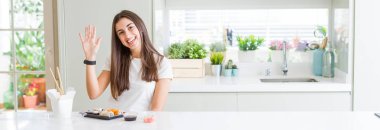 Doğumdan Asya suşisi yiyen güzel genç bir kadının geniş açılı fotoğrafı beş numarayı gösterip işaret ederken kendinden emin ve mutlu bir şekilde gülümsüyor..