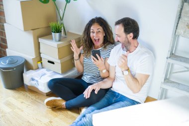 Orta yaşlı çift akıllı telefon kullanarak yeni bir eve taşınıyor. Gururla bağırıyor, zaferi ve başarıyı kutluyor. Çok heyecanlı, coşkulu bir duygu.