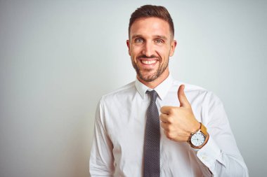 Soyutlanmış arka planda zarif beyaz gömlek giyen genç yakışıklı iş adamı mutlu bir el hareketi yapıyor. Kameraya bakıp başarıyı gösteren ifade onaylanıyor.