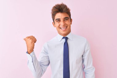 Genç yakışıklı işadamı gömlek ve kravat izole pembe arka plan üzerinde duran mutlu yüz görünümlü ve başparmak ile yan işaret gülümseyerek giyen.