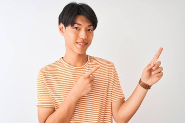 Izole beyaz arka plan üzerinde duran rahat çizgili t-shirt giyen genç Çinli adam gülümseyerek ve yan iki el ve parmakları ile işaret kamera bakıyor.