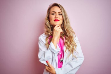 Pembe izole arka plan üzerinde steteskop kullanan genç ve güzel bir kadın kameraya kollarını kavuşturup gülümseyerek ve çenesini kaldırarak bakıyor. Olumlu düşünüyorum..