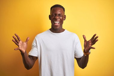 Beyaz t-shirt giyen genç Afro-Amerikalı adam izole edilmiş sarı arka planda duruyor ve kollarını kaldırmış, gözleri kapalı heyecanla haykırarak başarıyı kutluyor. Kazanan konsept