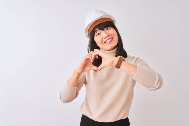 Genç, güzel bir Çinli mimar kadın, izole edilmiş beyaz arka plan üzerinde kask takıyor. Aşkla gülümsüyor. Elleriyle kalp sembolü ve şekli gösteriyor. Romantik konsept.