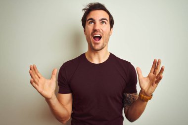 İzole edilmiş beyaz arka plan üzerine mor tişört giyen yakışıklı genç bir adam çılgın ve sinirli bir şekilde bağırıyor ve agresif bir ifade ve kolla bağırıyor. Hayal kırıklığı konsepti.