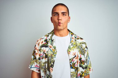 Tatilde olan yakışıklı bir genç, beyaz arka planda Hawaii gömleği giyip dudağında balık suratı yapıyor, çılgınca ve komik hareketler yapıyor. Komik ifade.