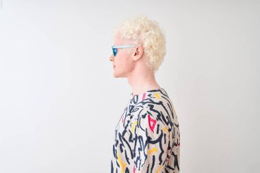 Renkli tişört ve güneş gözlüğü takan genç albino bir adam izole edilmiş kırmızı arka plan, rahat profil pozu, kendine güvenen bir gülümsemeyle doğal bir poz..