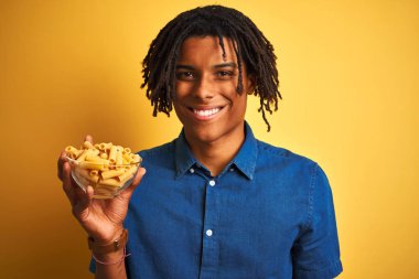 Sarı arka planda makarna tutan Afro-Amerikalı bir adam. Mutlu bir yüzü var ve gülümsüyor. Dişlerini gösteriyor.