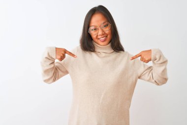 Balıkçı yaka kazak ve gözlük takan genç Çinli bir kadın izole edilmiş beyaz arka planda kendine güvenen, yüzünde bir gülümsemeyle kendini gururlu ve mutlu bir şekilde gösteren bir kadın..