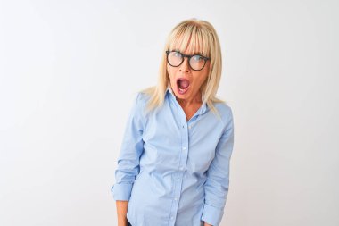 Orta yaşlı iş kadını zarif bir gömlek ve gözlük takıyor, beyaz bir arka planı var. Şok olmuş, şüpheci, alaycı ve ağzı açık bir şekilde bakıyor.