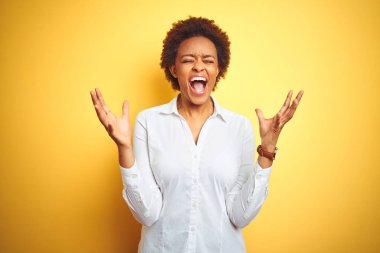 Afrika kökenli Amerikalı iş kadını sarı arka planda çılgın ve başarıyı kutluyor kollarını kaldırmış, gözlerini kapatmış heyecanlı çığlıklar atıyor. Kazanan konsept