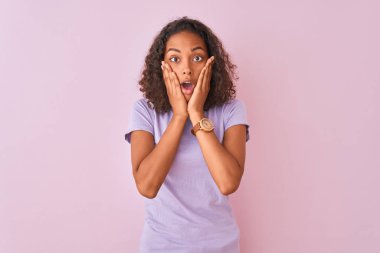 İzole edilmiş pembe arka plan üzerinde duran genç Brezilyalı kadın korkmuş ve şok olmuş, şaşırmış ve hayrete düşmüş bir yüz ifadesi var.